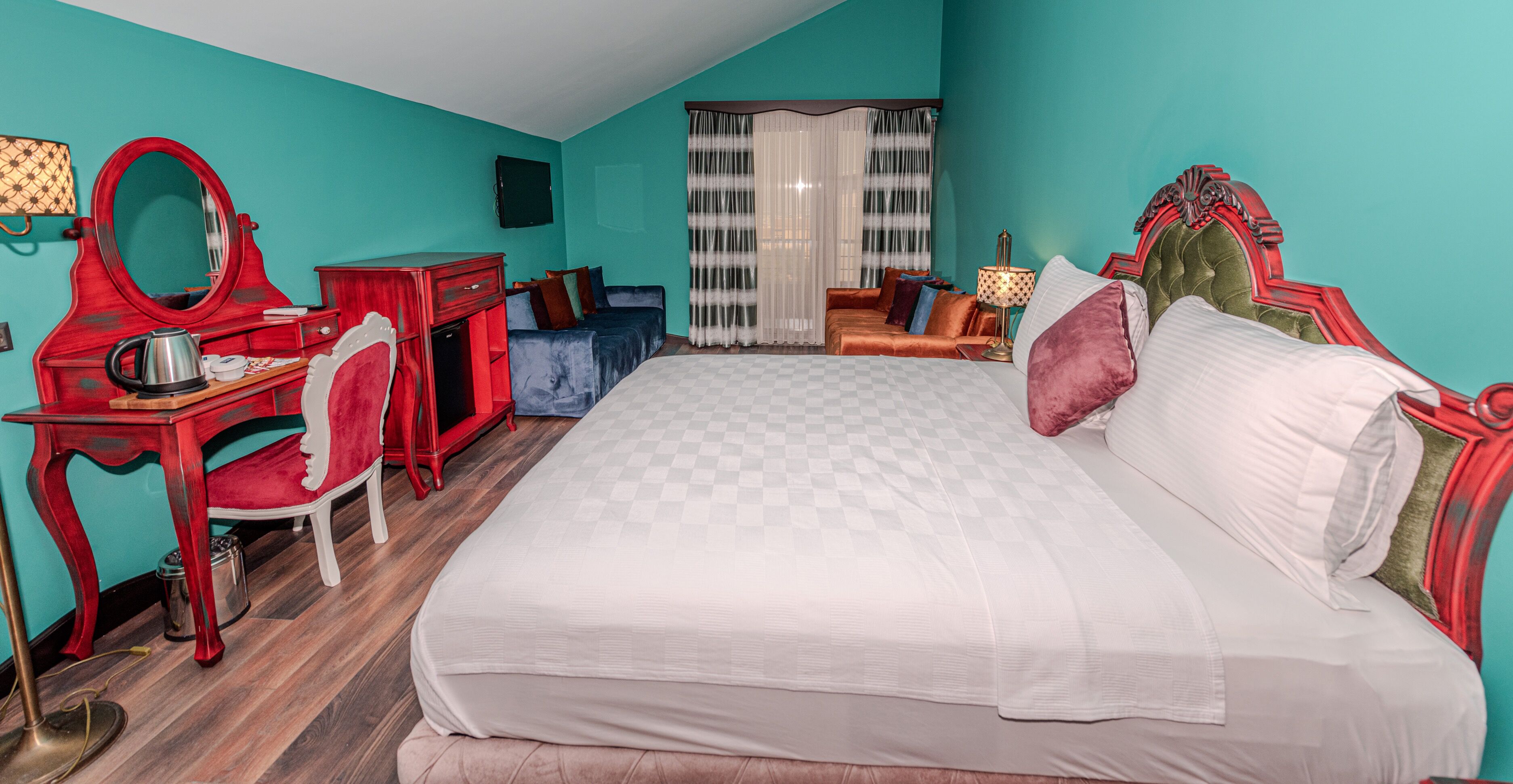 A bedroom with a large bed, a vanity with a mirror, a desk, and a window with curtains.