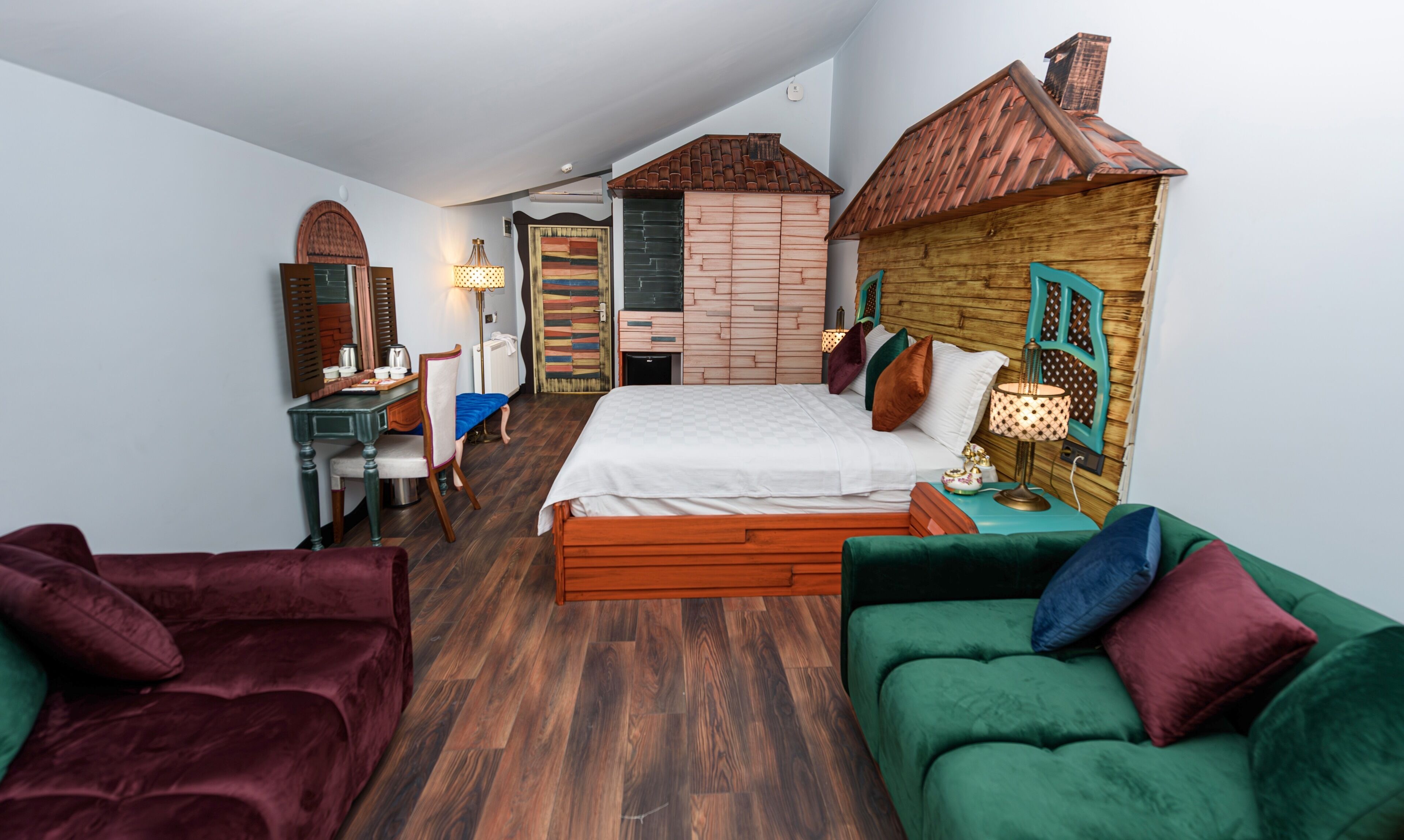A compact bedroom with a bed, a green sofa, a wooden headboard, a desk, and a chair.