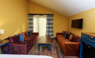 Habitación de hotel con un amplio sofá, una mesa de centro de madera y un televisor fijado a la pared.