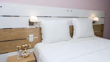 A neatly made bed with white linens, a wooden headboard, and bedside lamps.