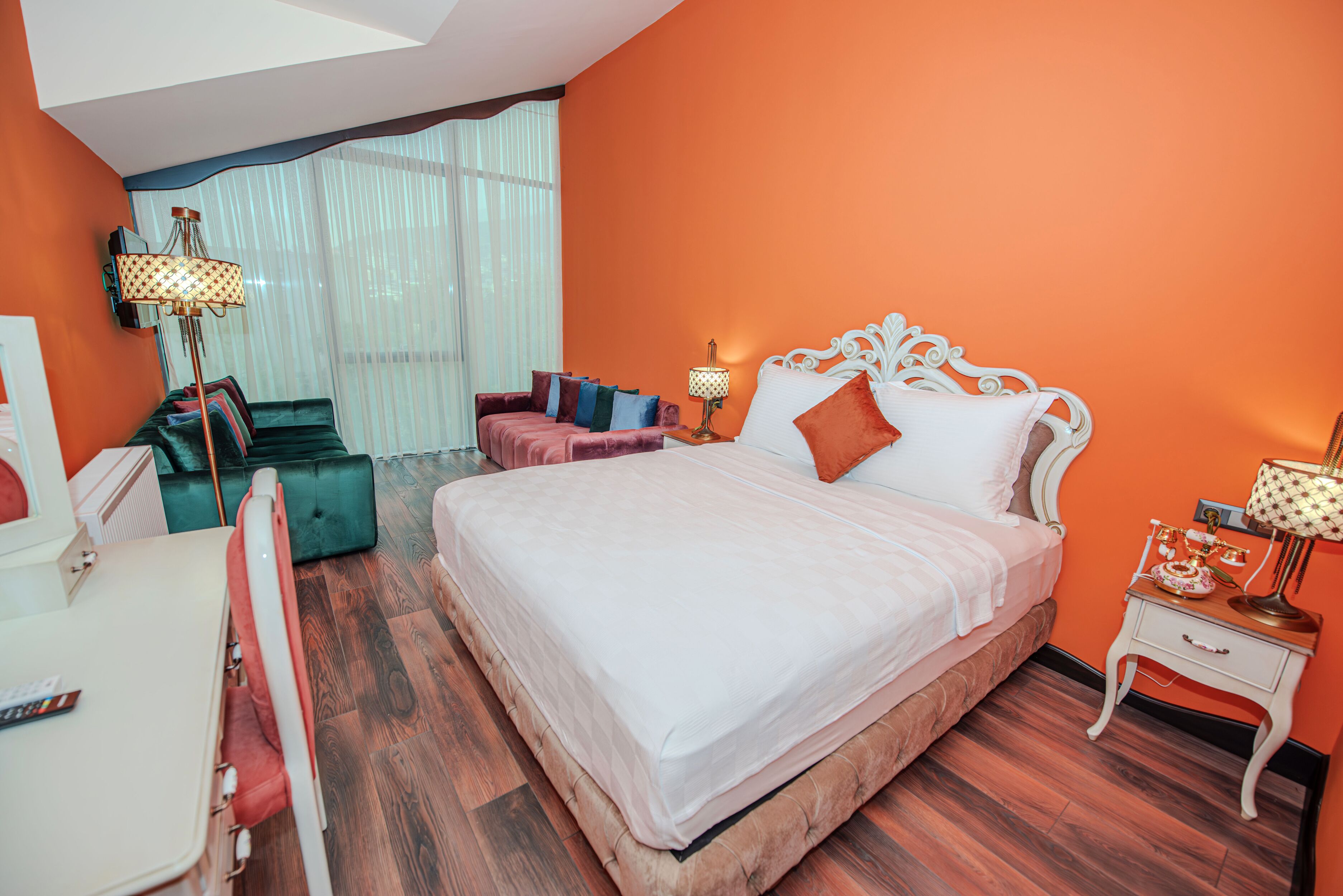 Een slaapkamer met een groot bed, een bureau, een stoel en een raam met gordijnen.