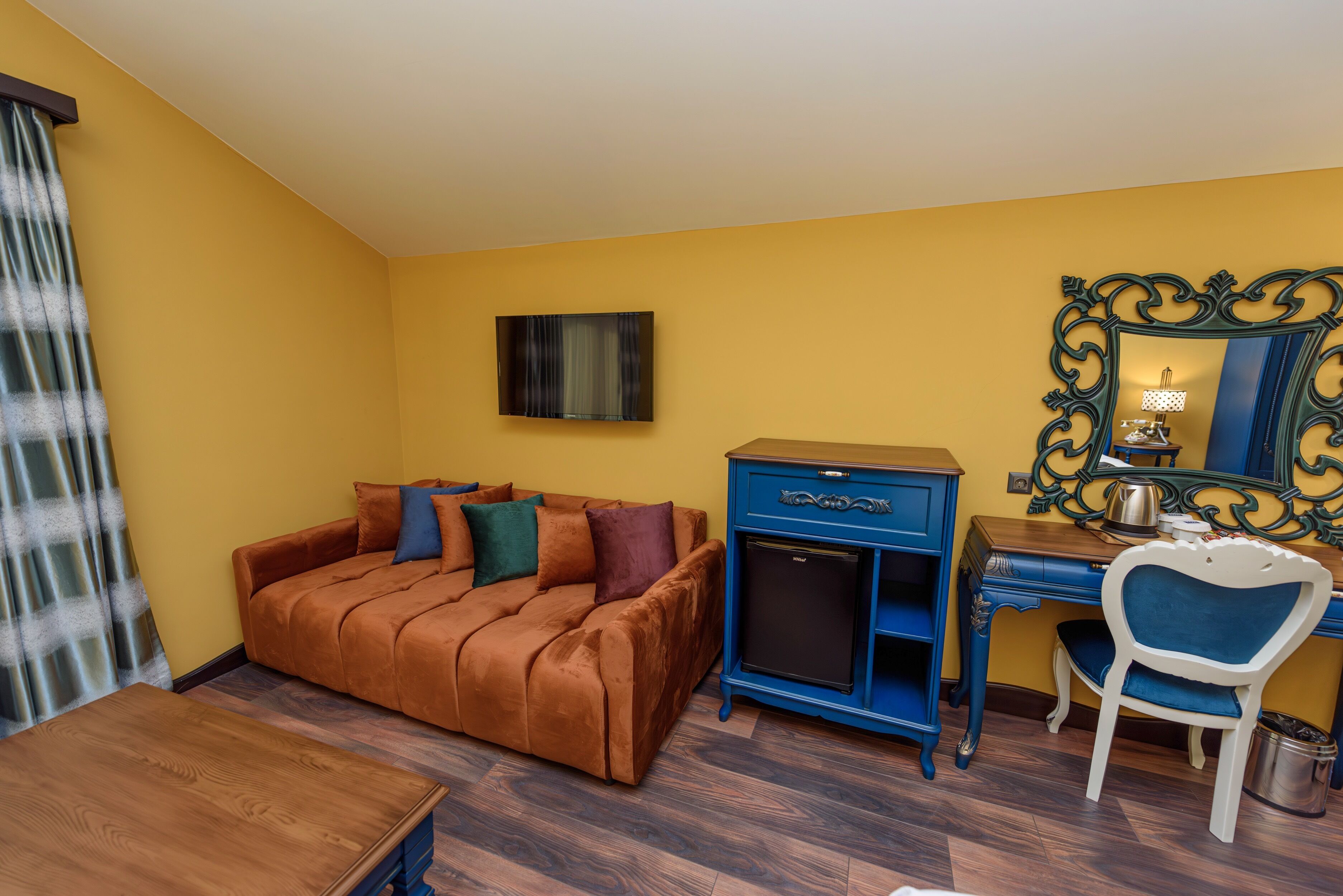 Una habitación con un sofá marrón, un armario azul, un escritorio de madera y una silla.