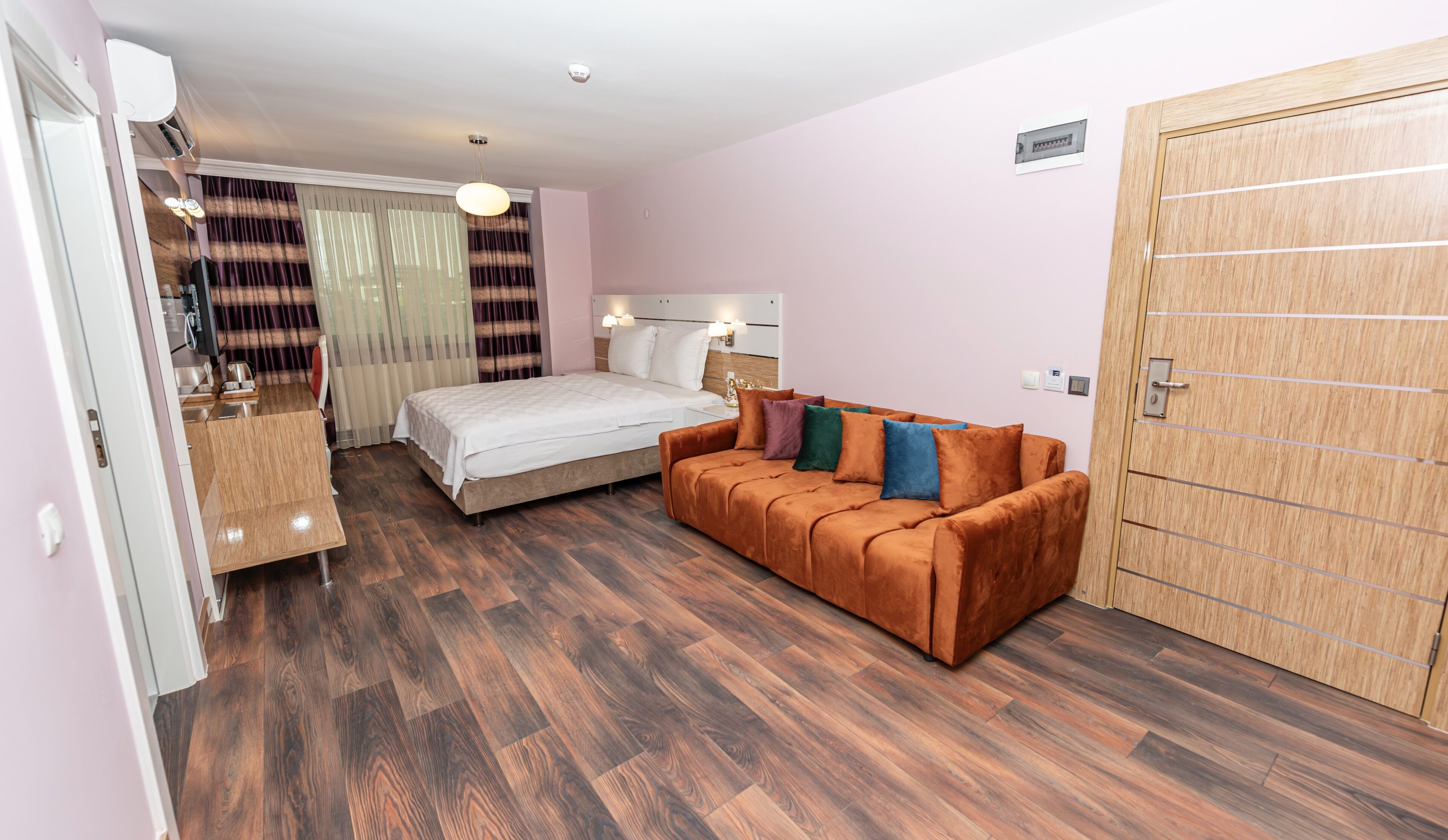 A hotel room with a bed, a sofa, a wooden wardrobe, and a desk with a chair.