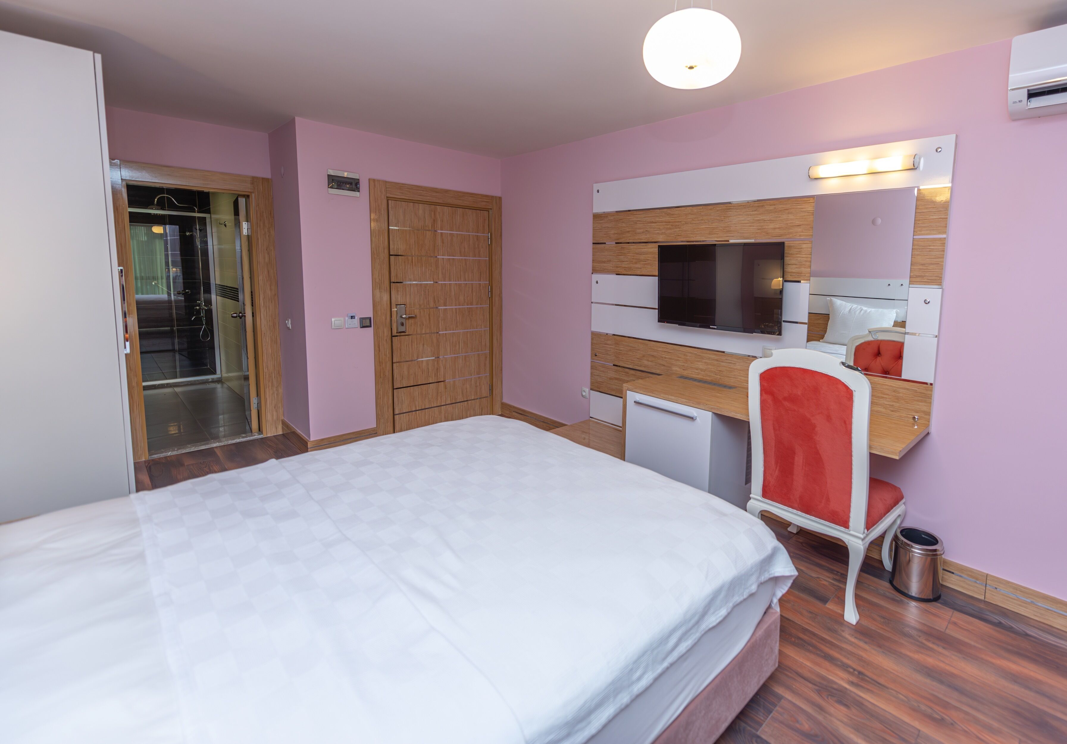 A hotel room with a bed, a desk with a chair, a TV, and a wardrobe.