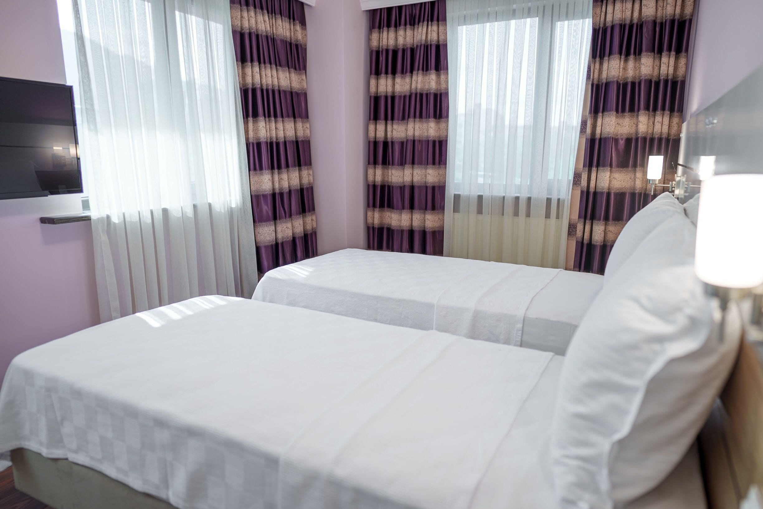 A hotel room with two beds, a flat-screen TV, and curtains.