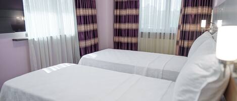 A hotel room with two beds, a flat-screen TV, and curtains.