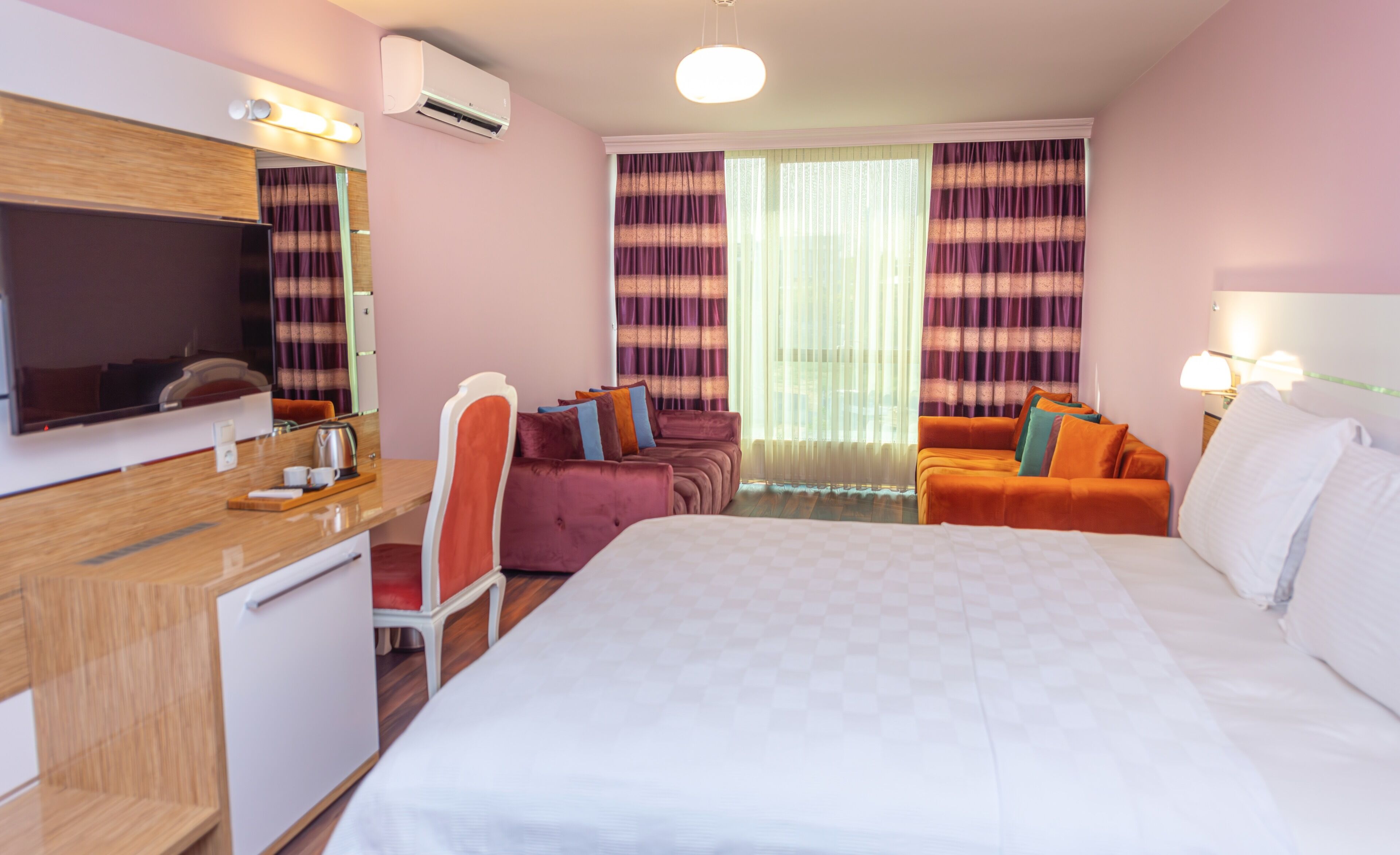 A hotel room with a bed, a desk with a chair, a television, and a sofa.