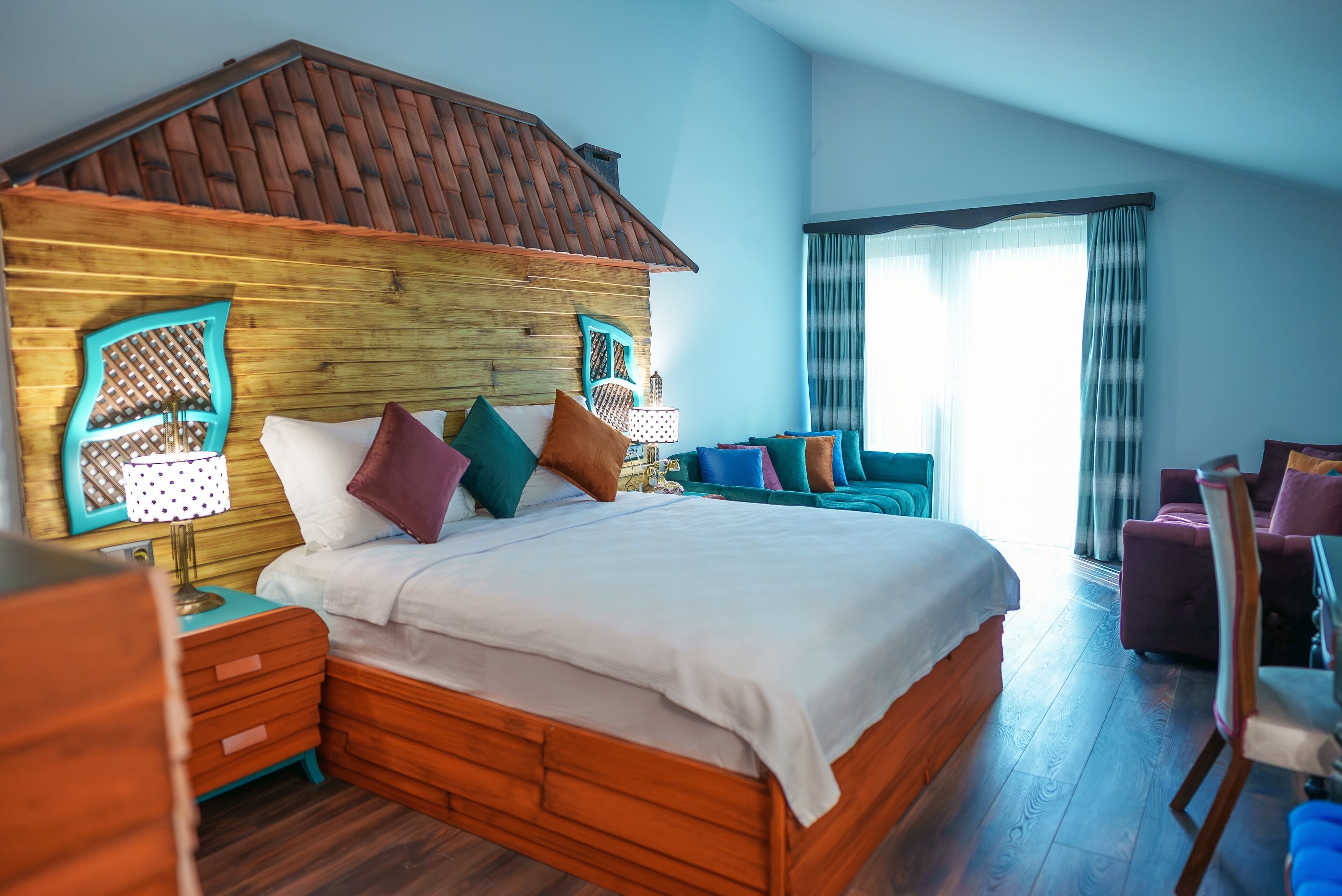 A bedroom with a wooden headboard, a large bed with multiple pillows, a nightstand, and a seating area with a chair and a small table.