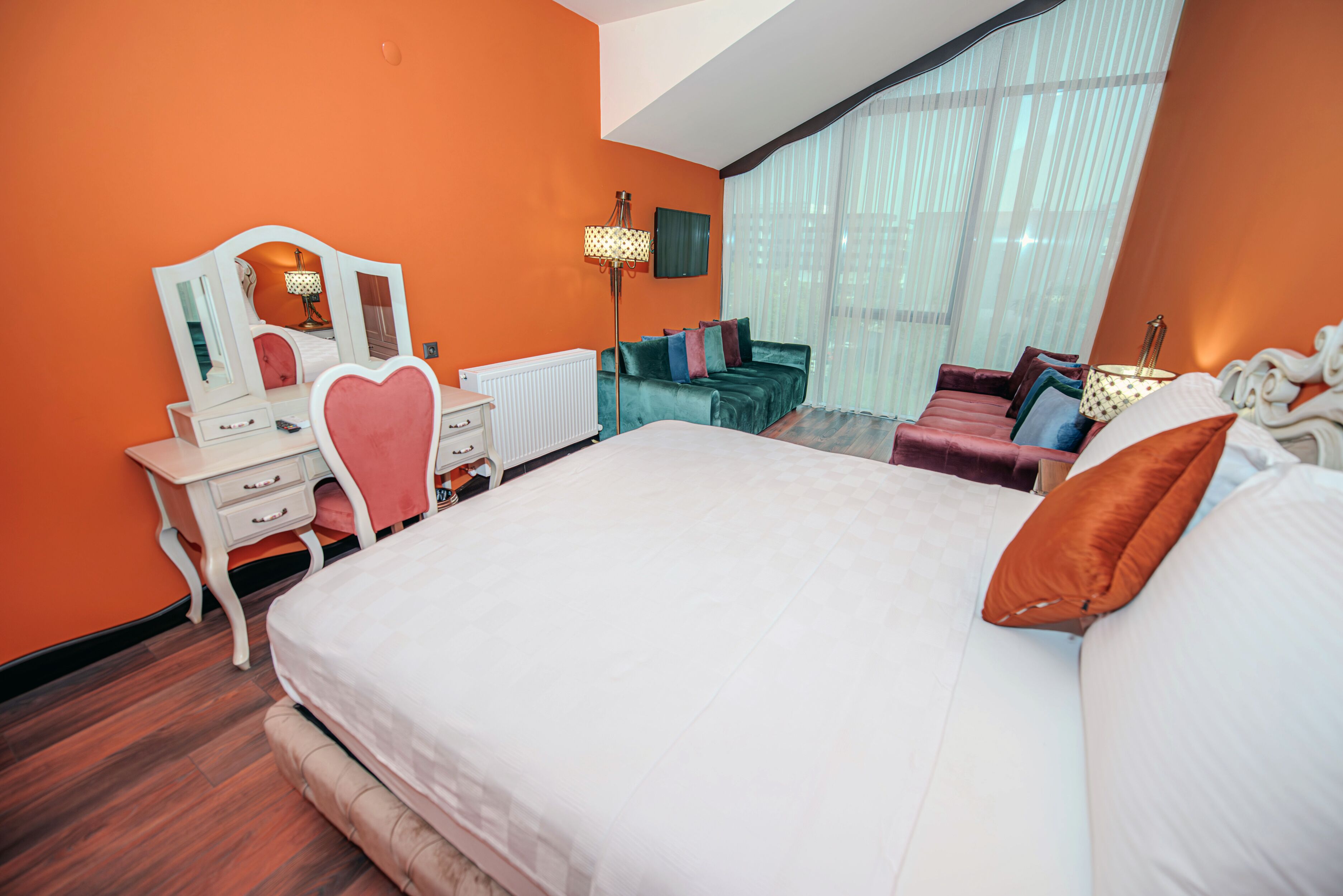 Una habitación de hotel con una cama grande, un tocador con espejo, un aparador y un área de descanso con sofá y cojines.