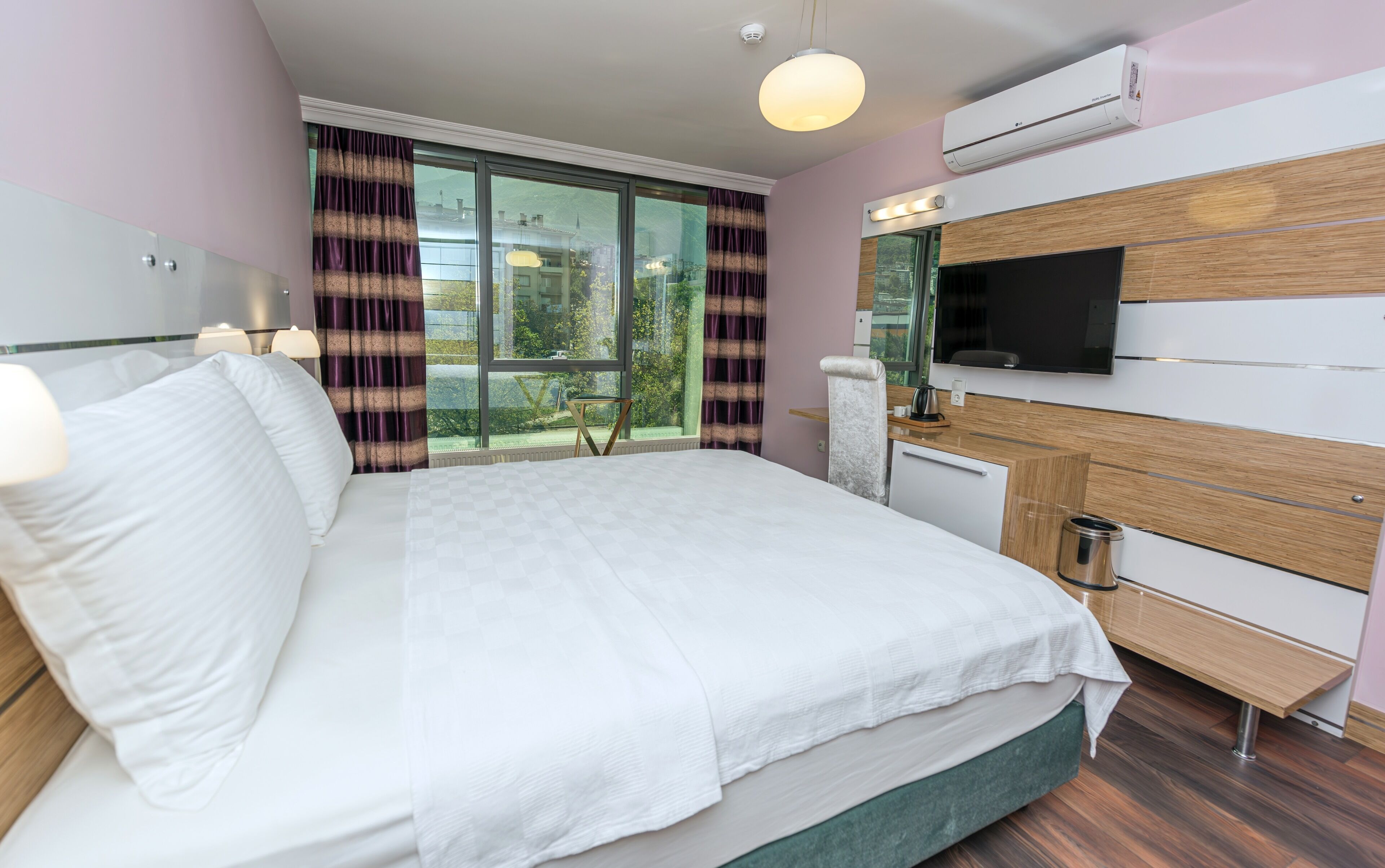A modern hotel room with a large bed, a TV mounted on the wall, and a window with curtains.