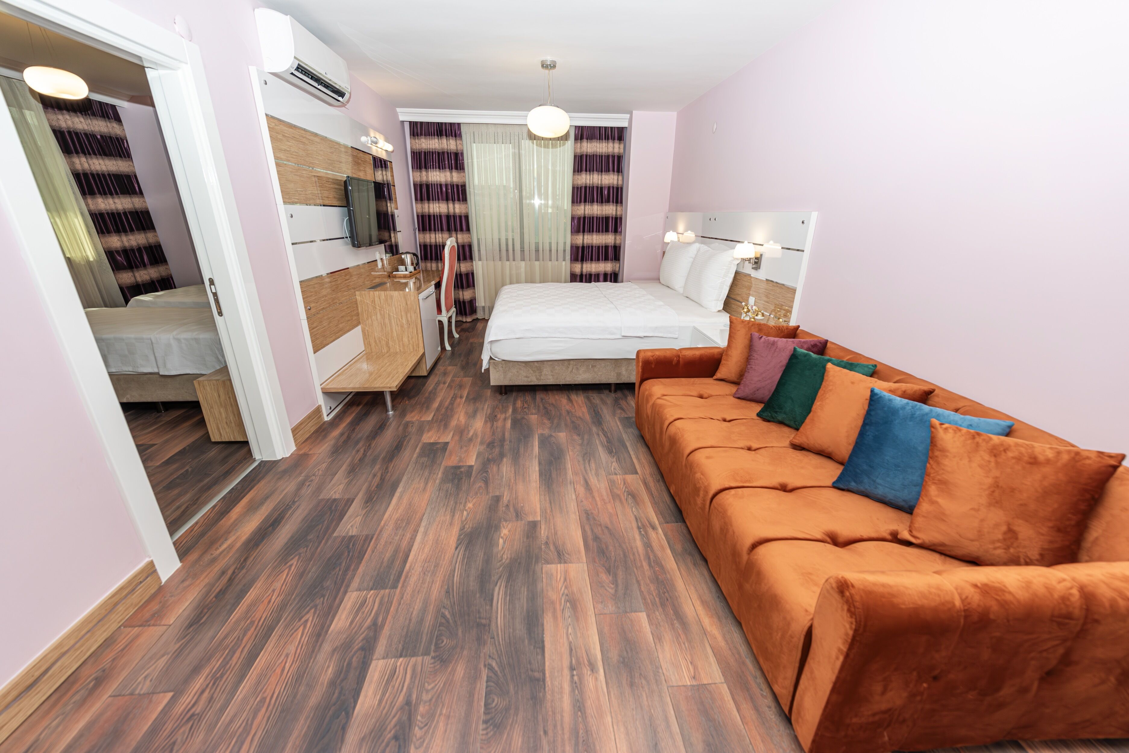 A modern hotel room with a bed, orange sofa, wooden flooring, and a small desk with a chair.