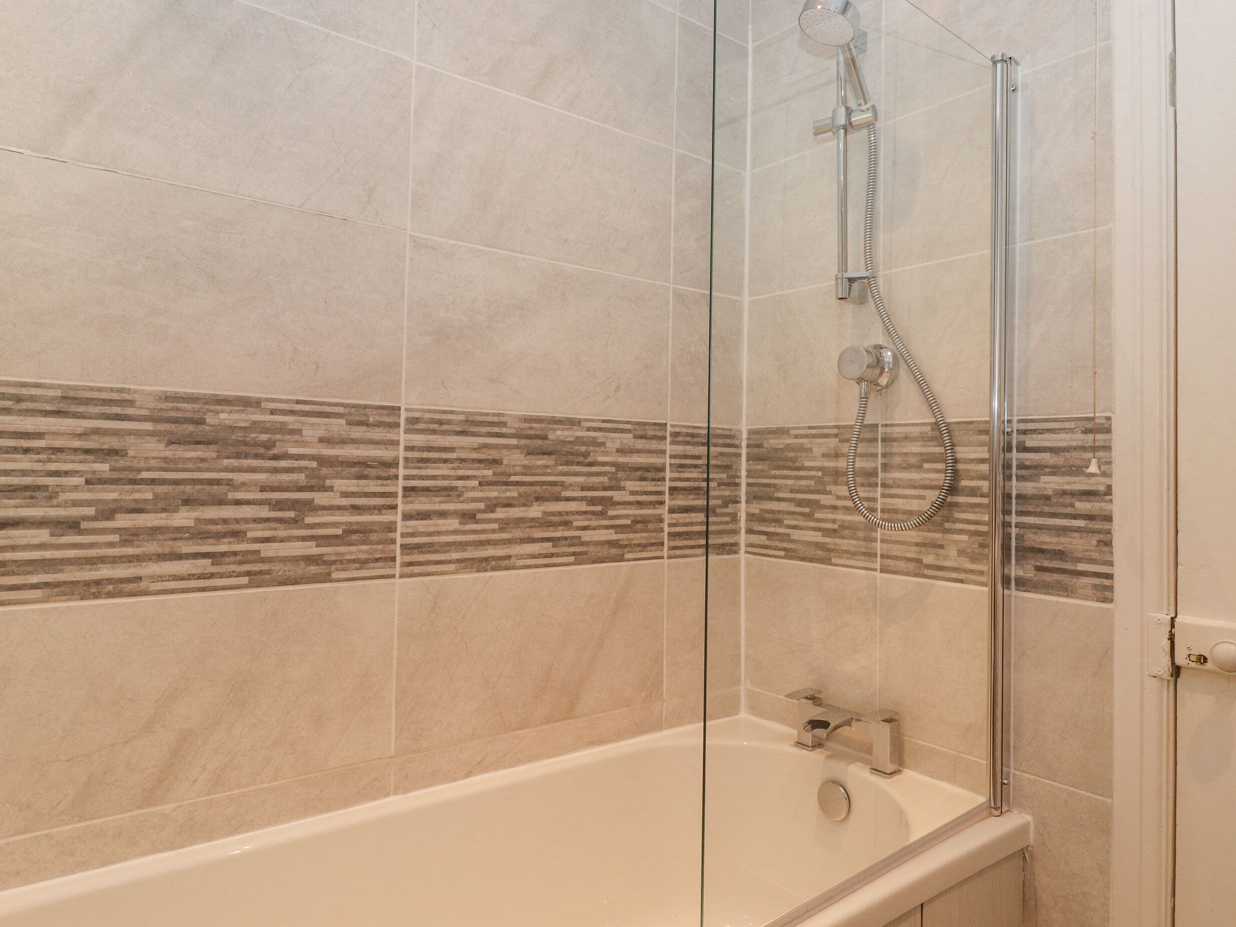 Un baño moderno con ducha de vidrio, una bañera y un muro de azulejos con diseño decorativo.