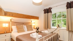 A neatly made bed with a brown quilt, a wooden headboard, and a bedside table with a lamp. - Riverbank (Ambleside)