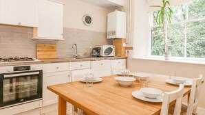 A modern kitchen with white cabinets, a wooden table, and a window with a view of trees. - Riverbank (Ambleside)
