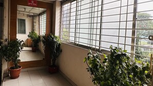 Ein Korridor mit Fliesenboden, Zimmerpflanzen, einem Deckenventilator und einem Fenster mit Gitterstäben.