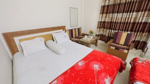 Ein Hotelzimmer mit einem Bett, einem kleinen Tisch mit Blumenvase, einem Sessel und einem Fenster mit Vorhängen.