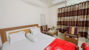 Ein Hotelzimmer mit einem Bett, einem kleinen Tisch mit Blumenvase, einem Sessel und einem Fenster mit Vorhängen.