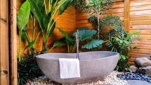 A stone basin with a towel, surrounded by pebbles and plants, in a wooden-walled area.