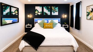 Une chambre moderne avec un lit, des tables de chevet, des œuvres d’art et un plaid noir.