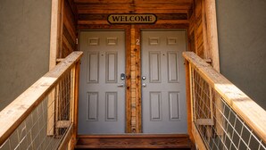 Un escalier en bois mène à une porte double, au-dessus de laquelle est affiché un panneau indiquant « BIENVENUE ».