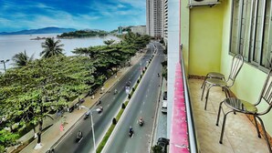 A balcony with a view of a busy road, a high-rise building, and a body of water. - Quang Vinh 2 Hotel (Bac Nha Trang)