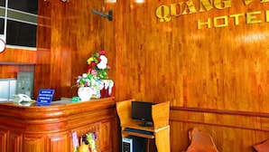 A wooden reception desk with a sign, a flower arrangement, and a television. - Quang Vinh 2 Hotel (Bac Nha Trang)