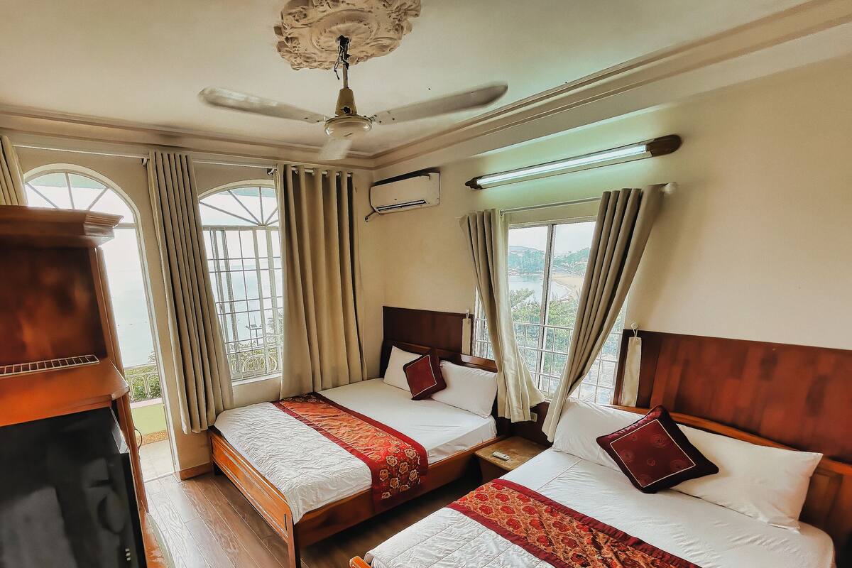 A hotel room with two beds, a ceiling fan, and large windows with curtains.
