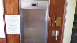 An elevator in a hotel with a wooden panel wall, a signboard, and a telephone. - Quang Vinh 2 Hotel (Bac Nha Trang)