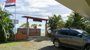 A gated entrance with a flag, a parked SUV, and a view of the sea.