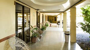 A corridor with wicker chairs and potted plants, leading to a room with a view.