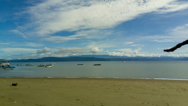 A beach with boats on the water and mountains in the background.
