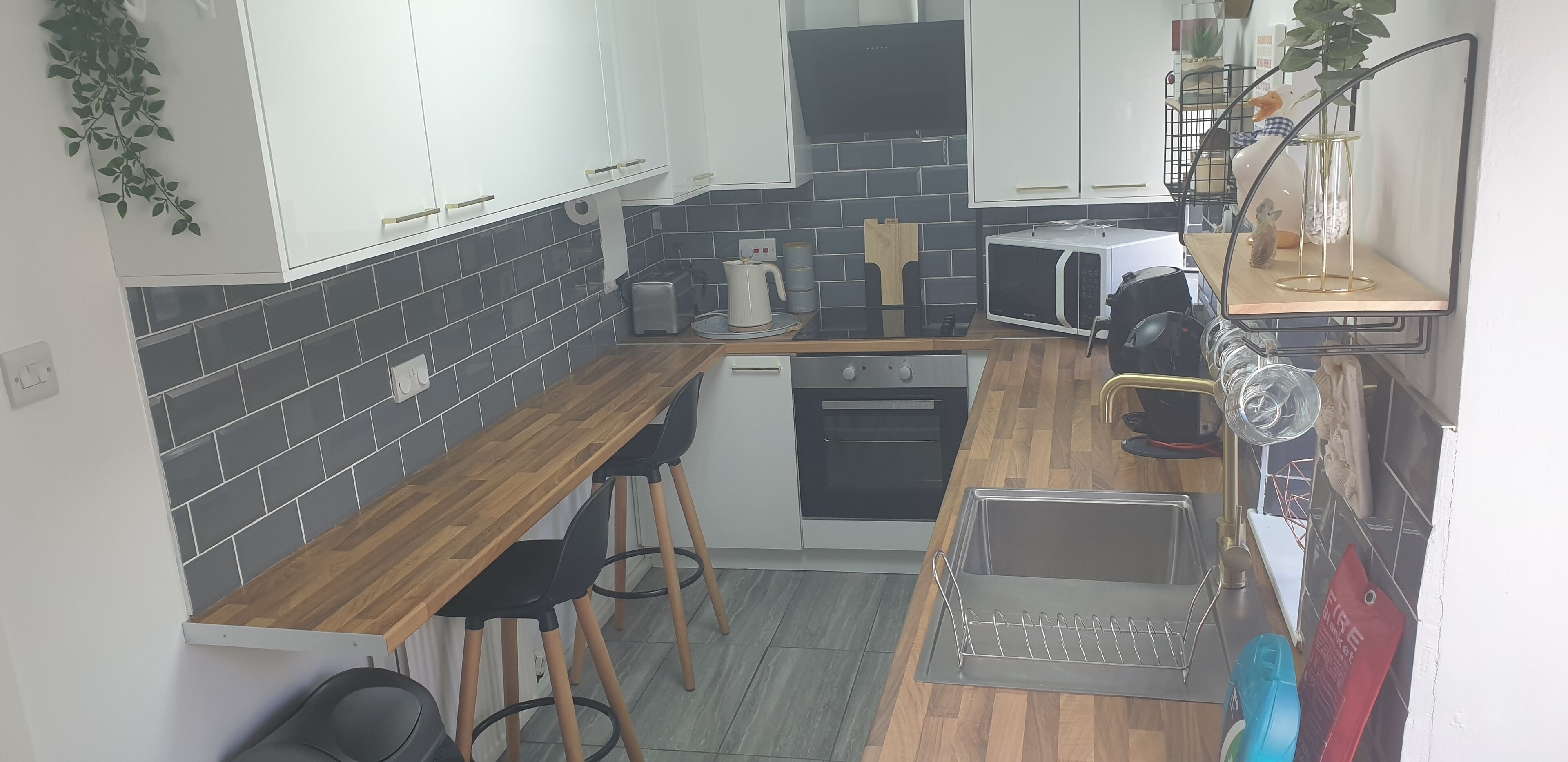 Una cocina compacta con encimera de madera, armarios negros y blancos, un microondas y un lavamanos.