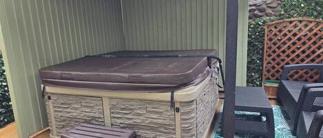 Una vasca idromassaggio con rivestimento in pietra, un molo di legno e mobili da esterno.