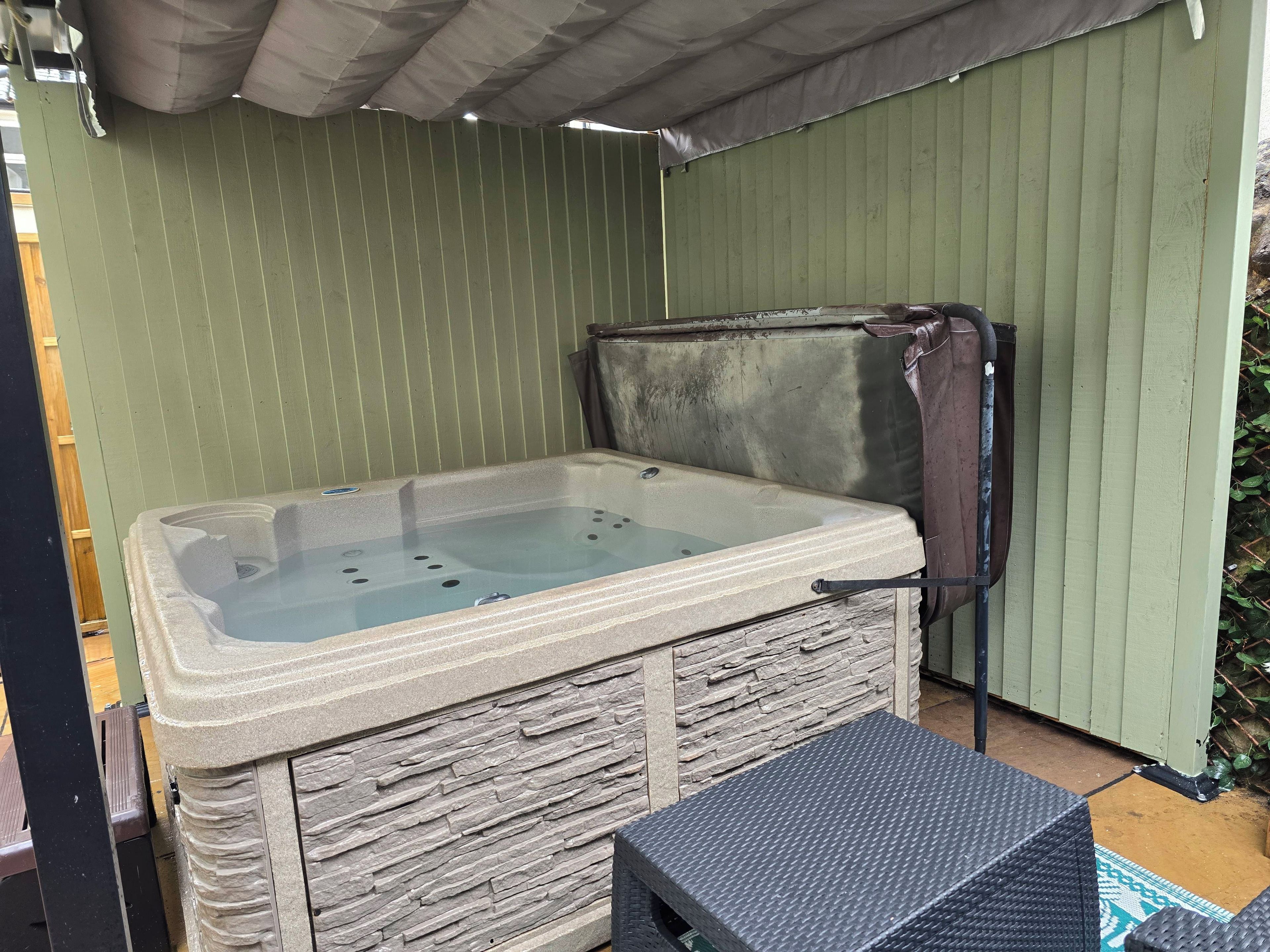 Una bañera de hidromasaje con revestimiento de piedra, estructura metálica y tapa de metal.