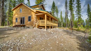 Une cabane en rondins dotée d’un porche et d’une cheminée, entourée d’une forêt.