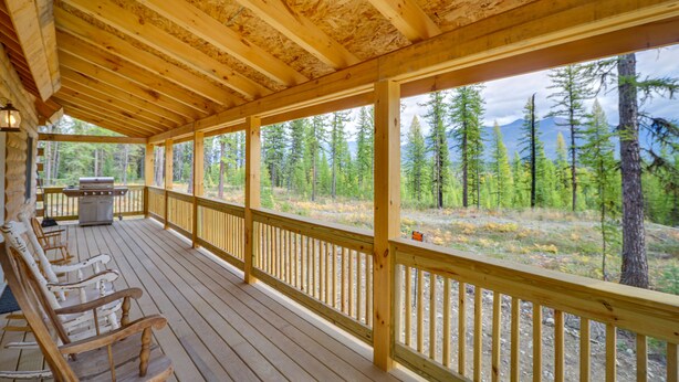 Une terrasse en bois avec un barbecue et des chaises, donnant sur une zone boisée avec des montagnes en arrière-plan.