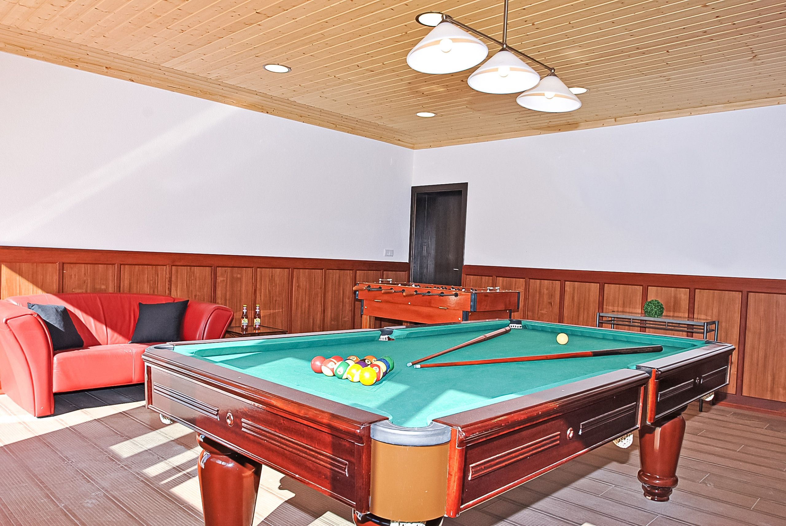 A pool table with balls, a red sofa, and wooden paneling on the walls.