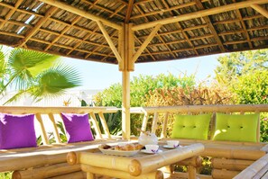 An outdoor seating area with bamboo furniture and cushions, a table with a teapot and cups, and a thatched roof structure. - Villa w/ BBQ and Pool in Albufeira (Albufeira)