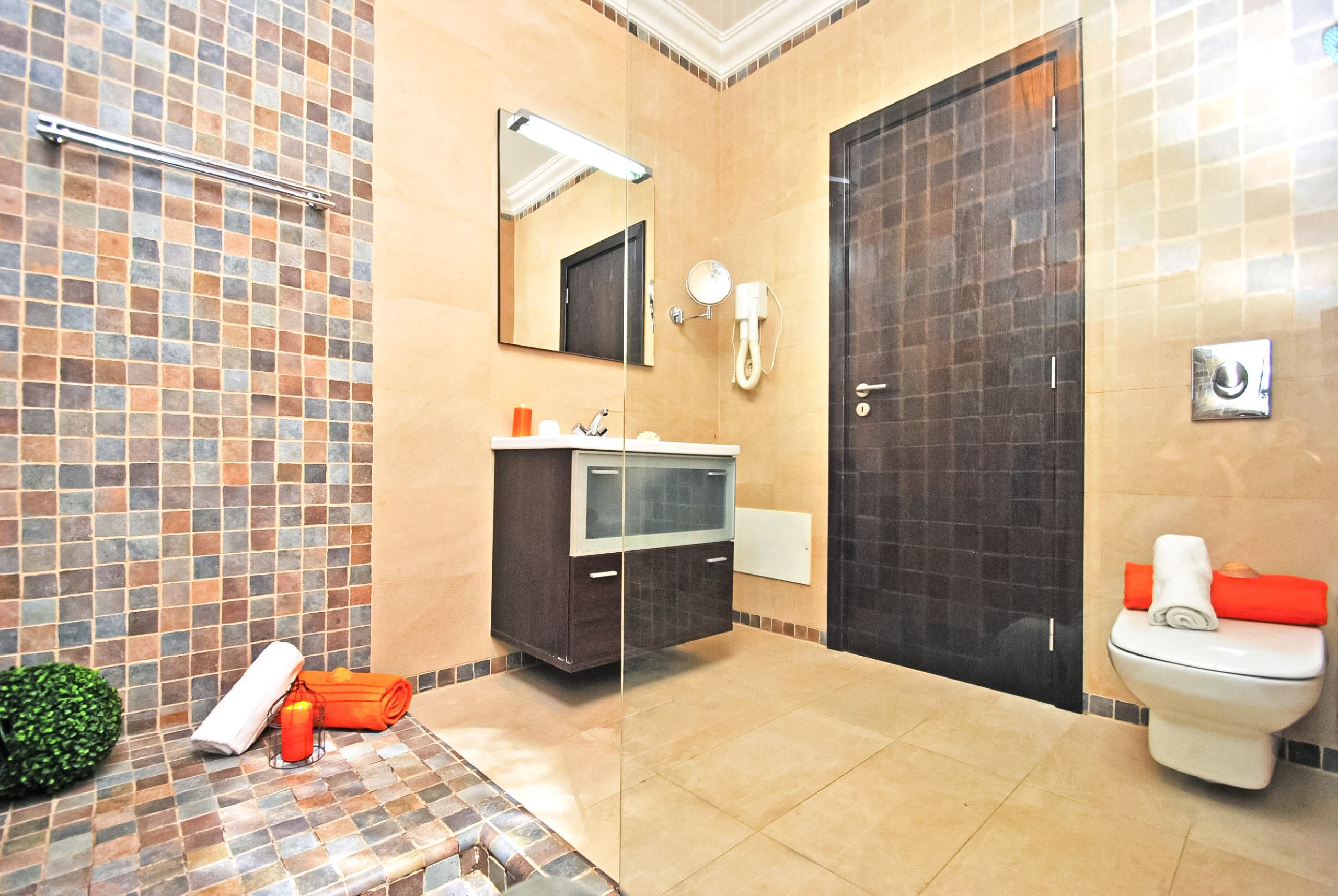 A bathroom with a tiled shower area, a sink with a mirror, a toilet, and a towel rack.