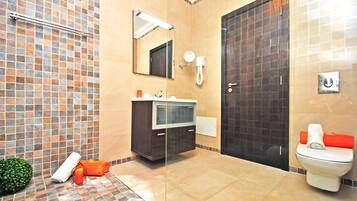 A bathroom with a tiled shower area, a sink with a mirror, a toilet, and a towel rack.