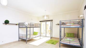 Una habitación con dos literas, una alfombra verde, una lámpara colgante y una pequeña planta en la pared.