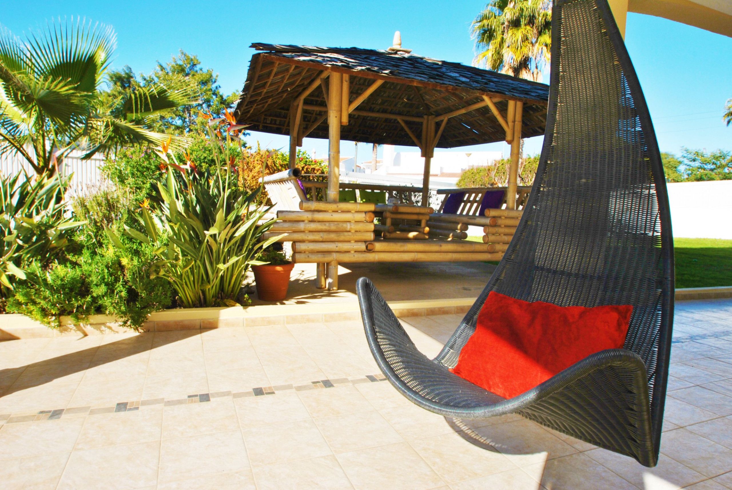 Un patio con una silla colgante, una pérgola de madera y plantas en macetas.
