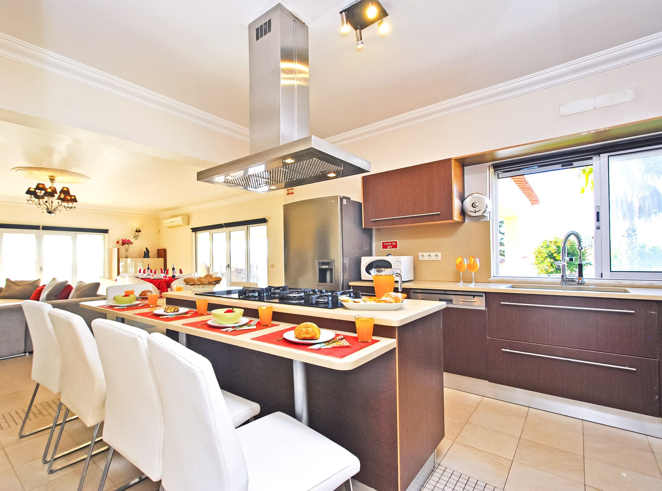 Una cocina moderna con una isla central, electrodomésticos de acero inoxidable y un comedor con sillas blancas.