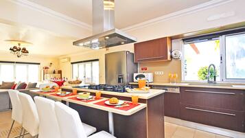 Una cocina moderna con una isla central, electrodomésticos de acero inoxidable y un comedor con sillas blancas.