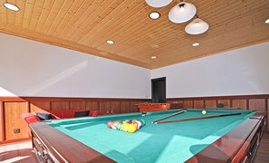 A pool table with balls, a red sofa, and wooden paneling on the ceiling.
