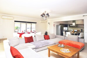 A modern living room with a sofa, a coffee table, and a dining area with a table set for four. - Villa w/ BBQ and Pool in Albufeira (Albufeira)