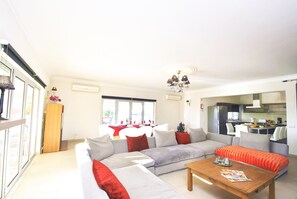 A modern living room with a sectional sofa, a wooden coffee table, and a dining area with a red tablecloth. - Villa w/ BBQ and Pool in Albufeira (Albufeira)