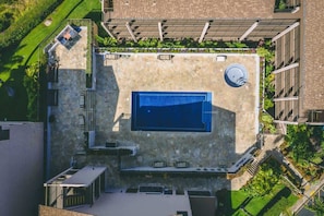 An aerial view of a rooftop with a swimming pool, stone flooring, and surrounding greenery.