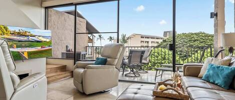 Ein modernes Wohnzimmer mit großem Fenster, einer Couch, einem Relaxsessel und einem Flachbildfernseher.
