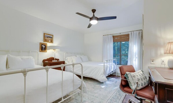 A room with two single beds, a desk, a chair, a ceiling fan, and a window with curtains.